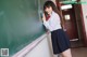 A woman in a school uniform leaning against a blackboard.