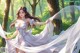 A woman in a white dress is dancing in the woods.