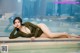 A woman in a green bodysuit laying on the edge of a pool.