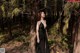 A woman in a black dress standing in the woods.