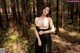 A woman in a black dress standing in the woods.