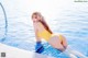 A woman in a yellow bathing suit sitting on the edge of a swimming pool.